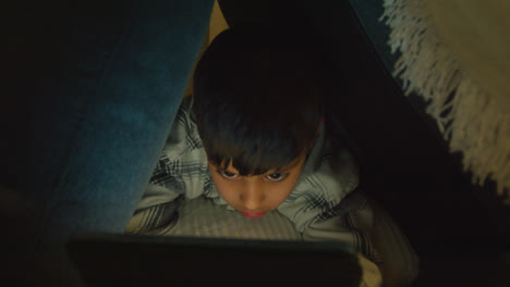 Close-Up-Of-Young-Boy-In-Home-Made-Camp-Made-From-Cushions-Playing-With-Digital-Tablet-At-Night-1